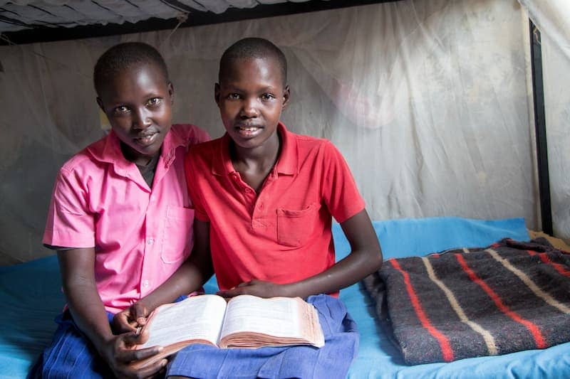 Two children sitting on a bed, reading together, embodying education and friendship in a shared learning environment.