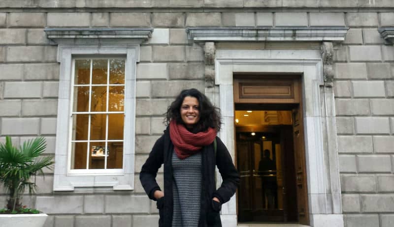 Woman smiling in front of a historical building with a red scarf.