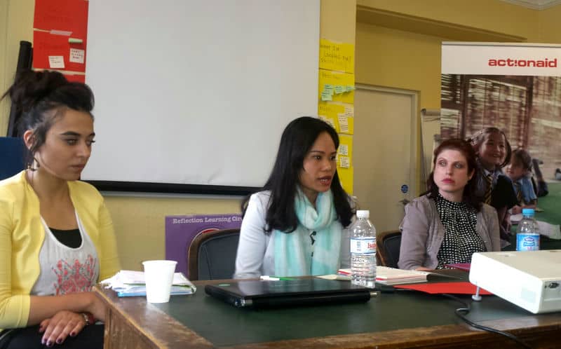 Three women engaged in a panel discussion at a conference, with notes and a screen in the background.