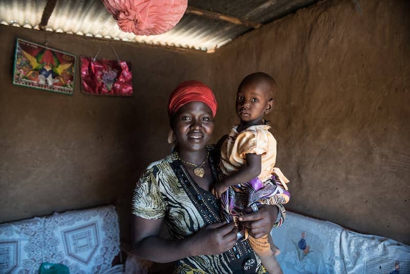 Mother holding child in room with red lamp, showcasing love and warmth in a rustic setting.