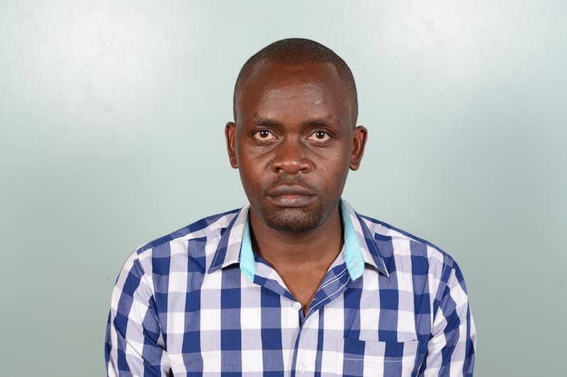 Man in a blue checkered shirt against a plain background, looking directly at the camera.