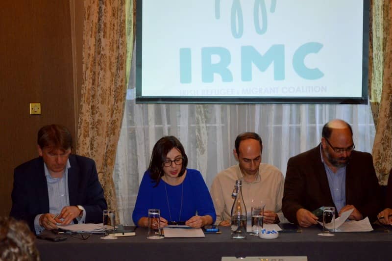 Panel discussion at IRMC meeting with four people engaged in paperwork and conversation, focus on refugee issues.