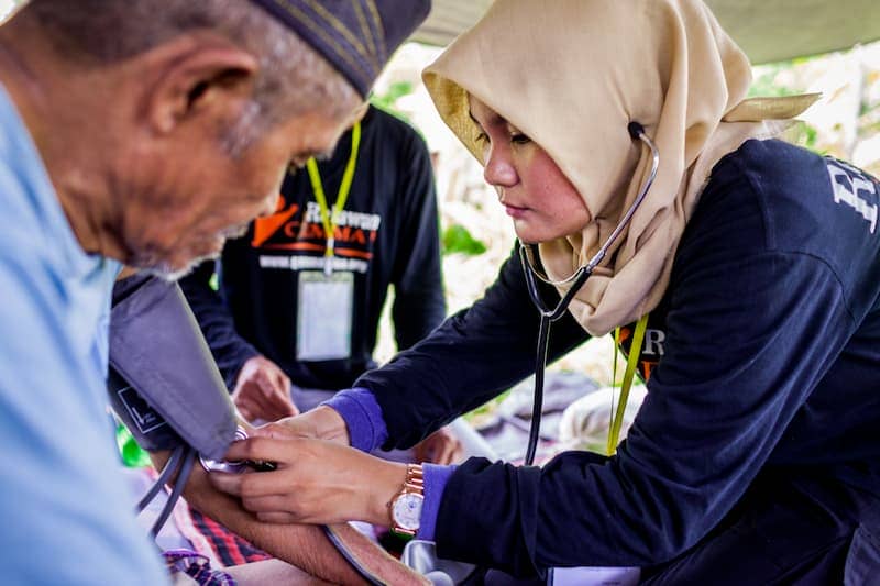 Healthcare worker checking blood pressure of an elderly man outdoors.