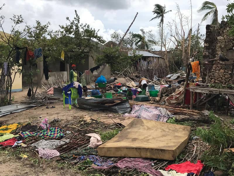 Destruction aftermath of a cyclone with scattered debris, damaged homes, and clothes drying amidst recovery efforts.