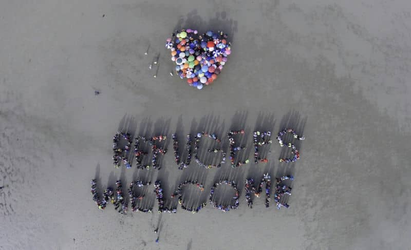 Aerial view of group forming REFUGEES WELCOME with a heart symbol on sandy ground, promoting inclusivity and unity.