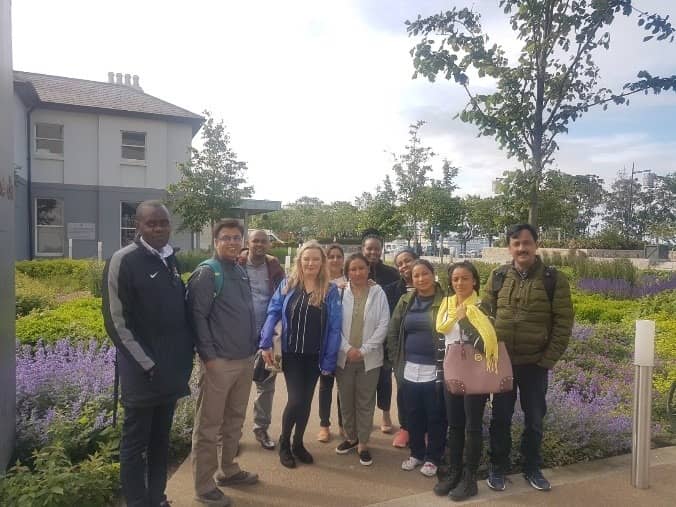 A group of people standing outside a building surrounded by greenery and flowers on a sunny day.