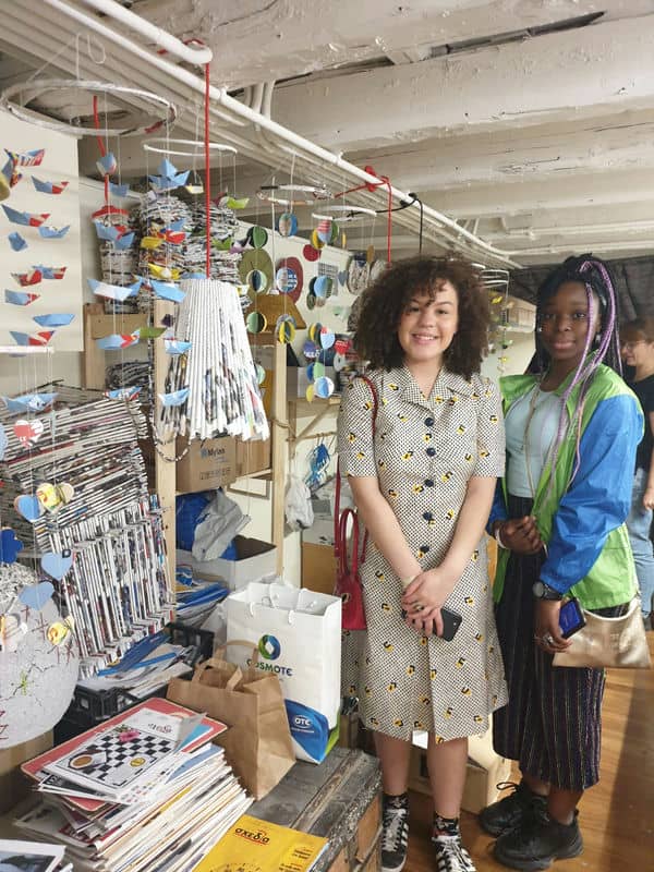 Two people smiling in an art studio with colorful paper crafts and hanging decorations.
