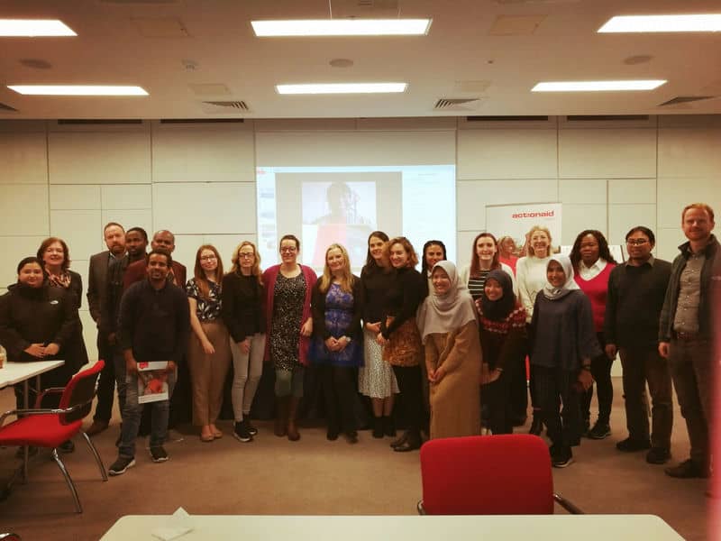 Group of diverse professionals posing together in a conference room with a presentation screen in the background.