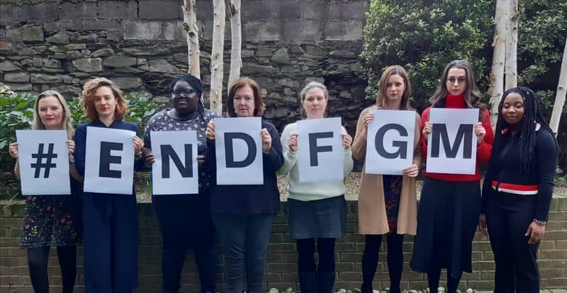 People holding signs reading #ENDFGM to raise awareness against female genital mutilation outdoors.