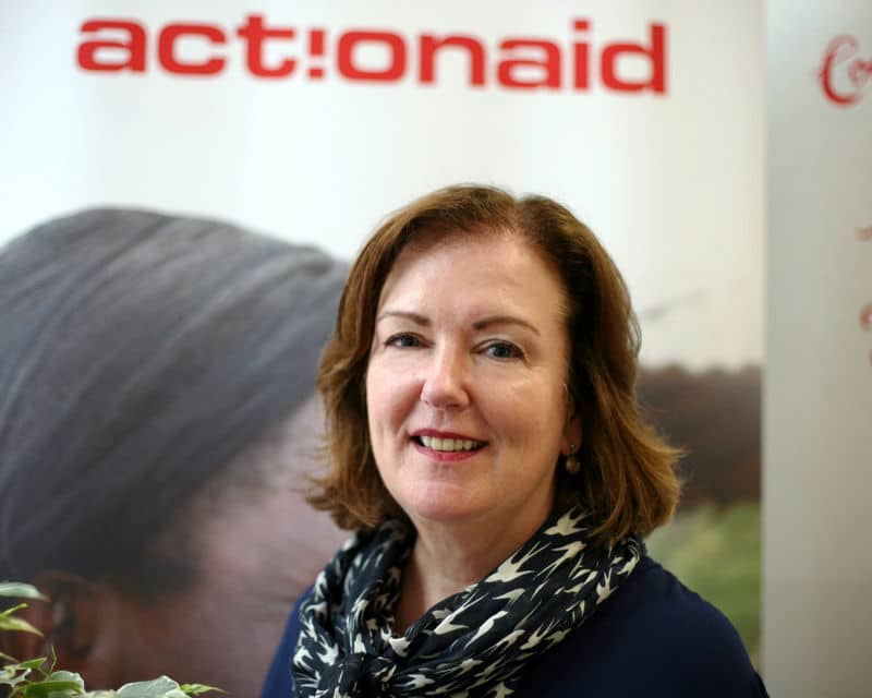 Woman smiling in front of ActionAid banner, wearing a patterned scarf.