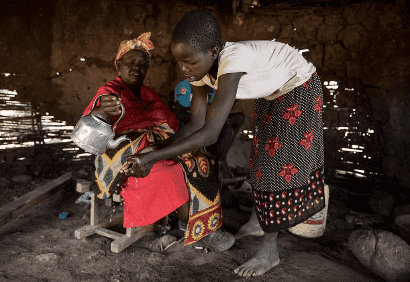 A woman pouring water over a child's hands in a rustic setting, highlighting cultural traditions and daily life.