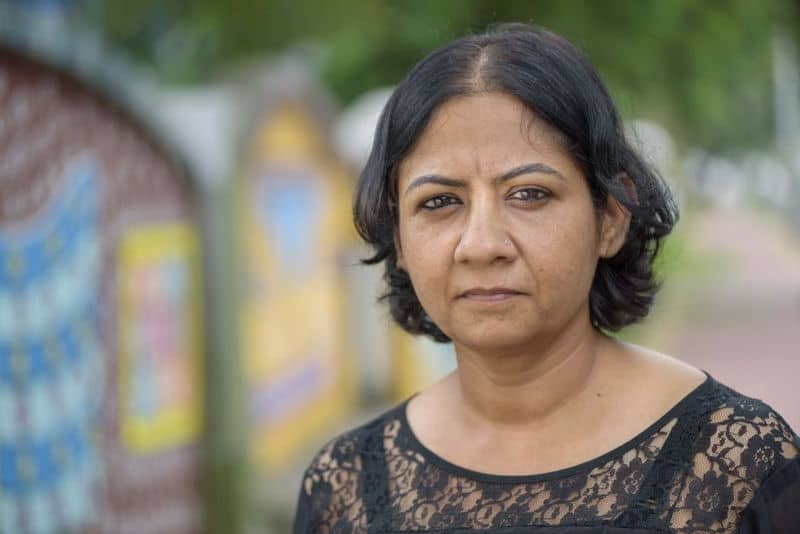 Woman outdoors in a decorative setting, wearing a lace top, with a thoughtful expression.