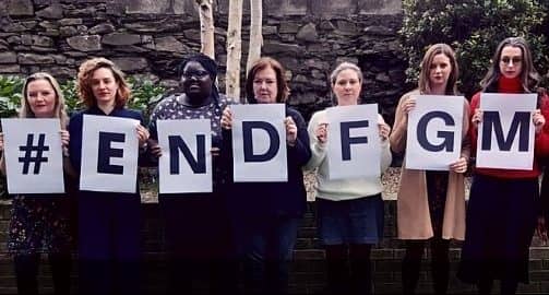 Group holding signs that spell #EndFGM advocating against female genital mutilation in front of a brick wall.