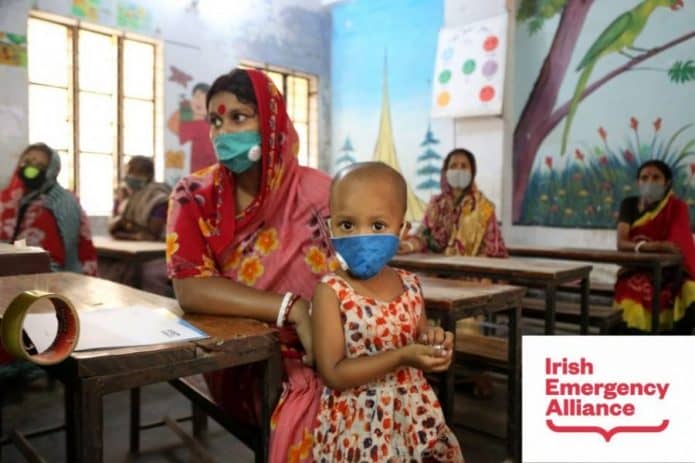 Women and children in masks sit in a colorful classroom, supported by Irish Emergency Alliance.