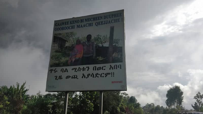 Billboard in rural Ethiopian landscape with local language text, cloudy sky background.