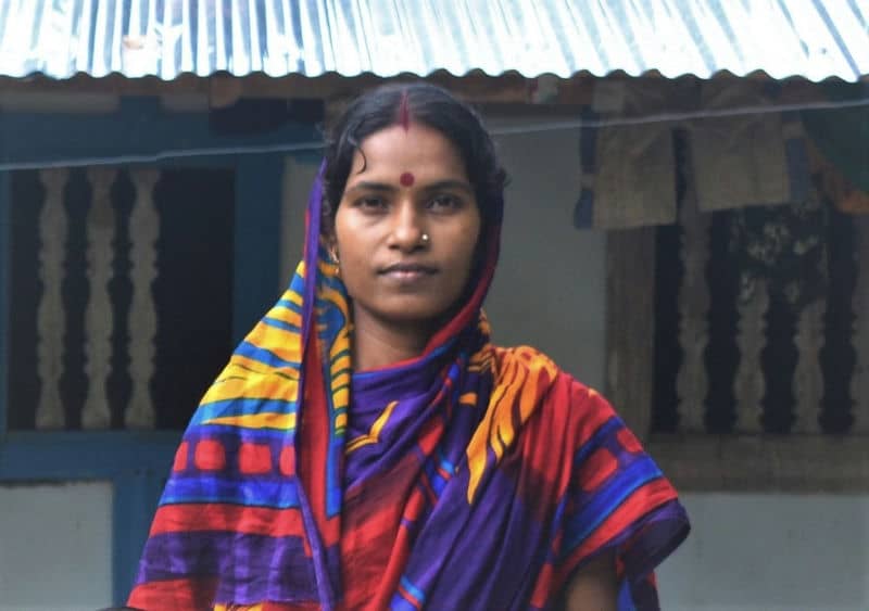 Woman in colorful sari standing outside under a corrugated roof.