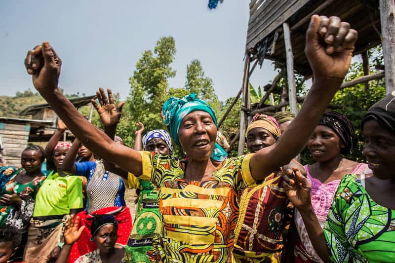 Women in vibrant attire celebrate outdoors, raising arms in joy, embodying community and cultural spirit.