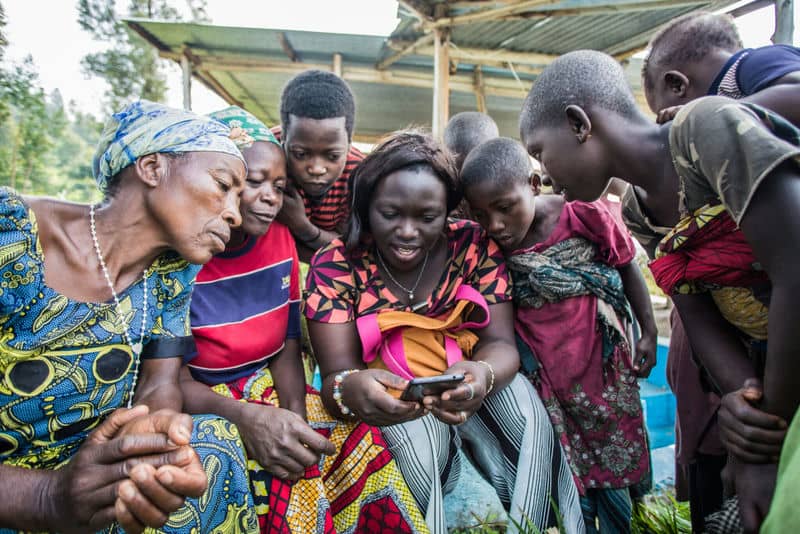 Group of people eagerly looking at a smartphone, sharing a moment of connection and curiosity outdoors.
