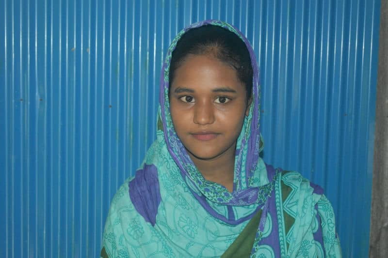 Young woman in a blue and green patterned scarf against a blue corrugated background, looking at the camera.