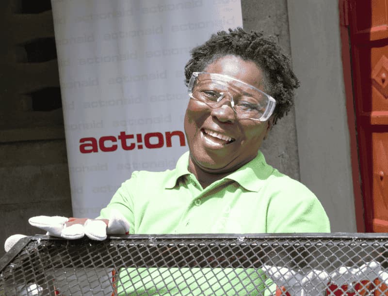 Smiling person in safety goggles and gloves showcasing an action project outdoors with a banner in the background.