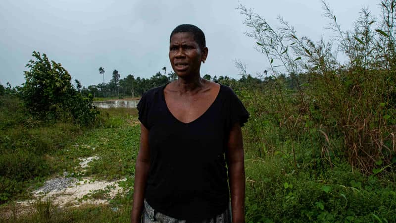 Woman standing in lush green field with overcast sky, representing rural lifestyle and nature connection.