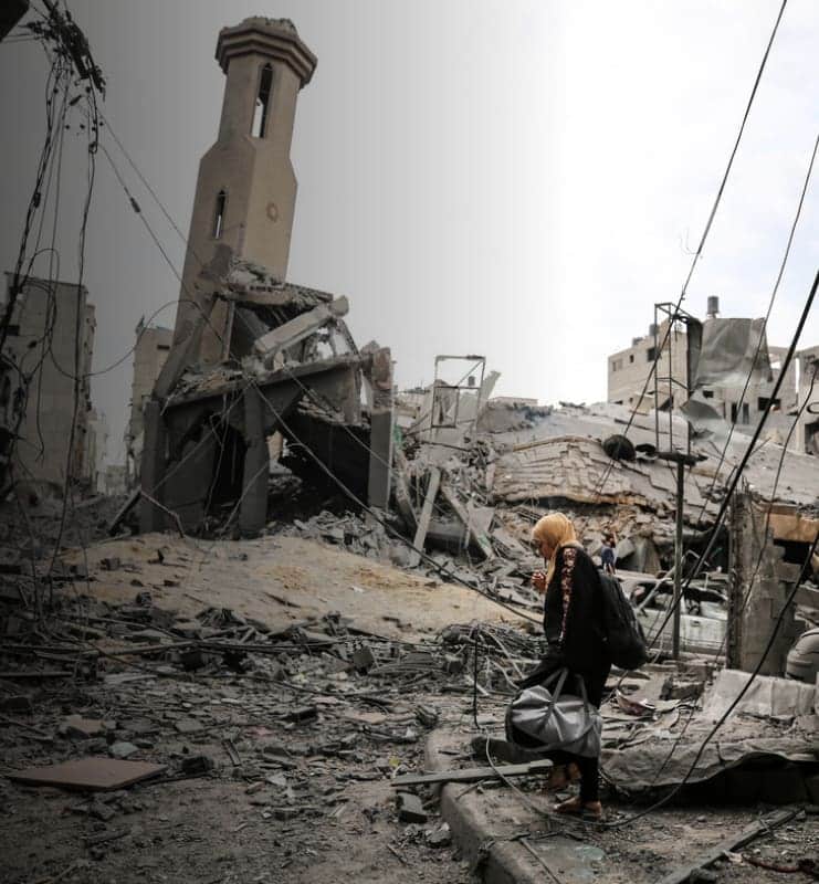 Woman walking through a devastated urban landscape with a damaged building in the background, showcasing war impacts.