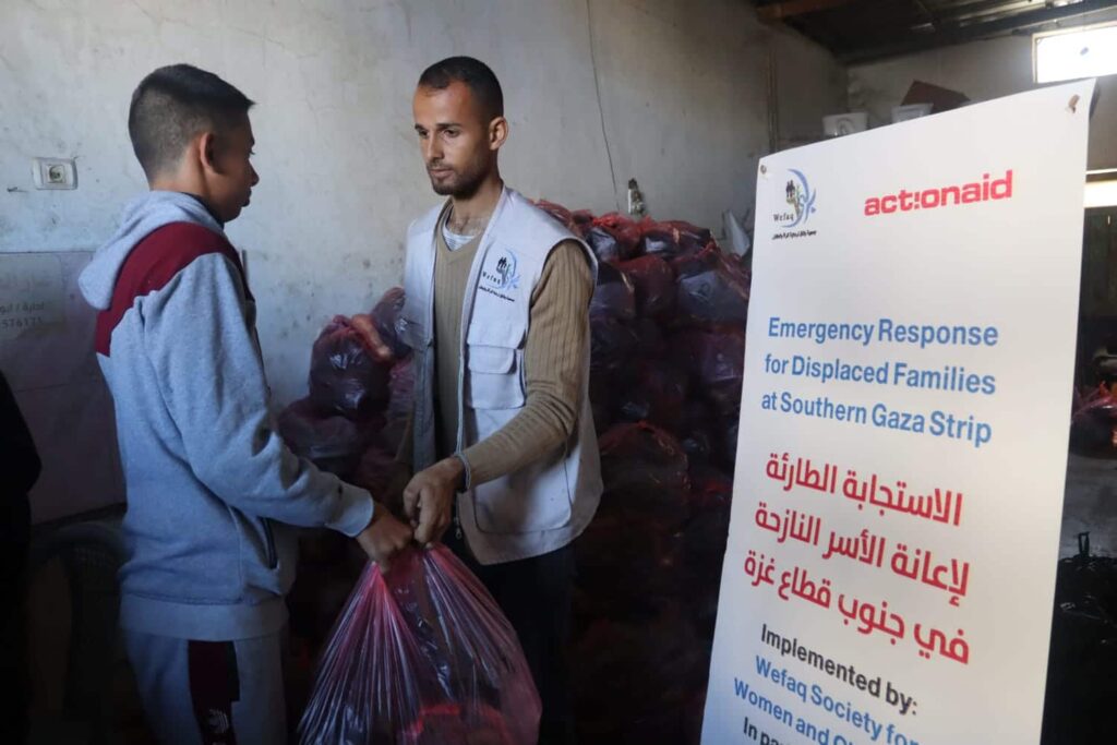 Humanitarian aid distribution in Gaza: worker handing bag to recipient beside emergency response sign.