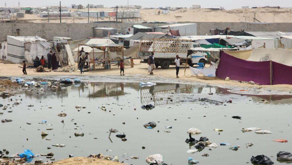 Informal settlement with tents and puddles, showcasing poor living conditions and environmental challenges.