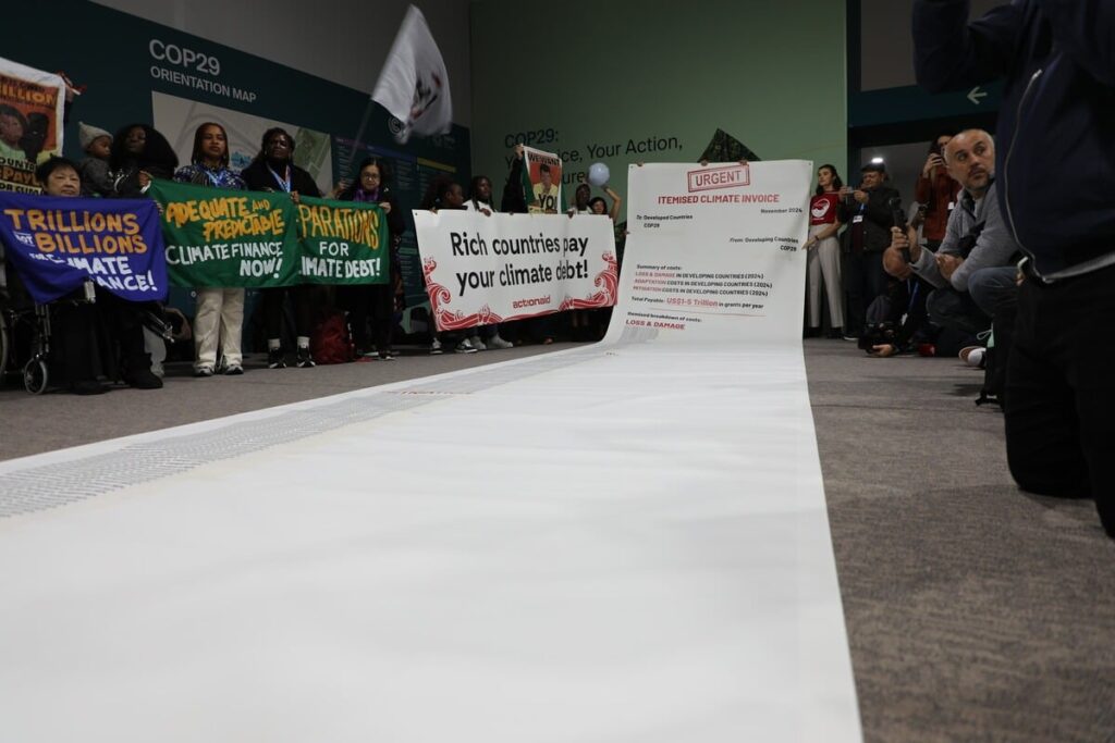 Climate activists at COP29 with banners demanding climate debt repayment from rich countries.