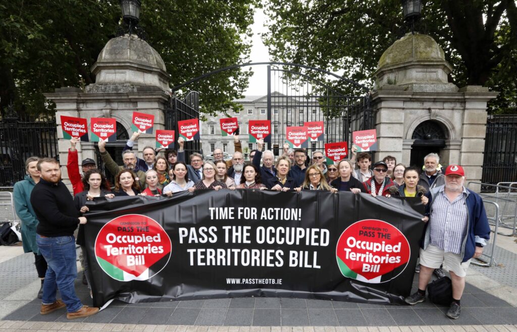Protesters holding signs for the Occupied Territories Bill outside government building, advocating for legislative action.