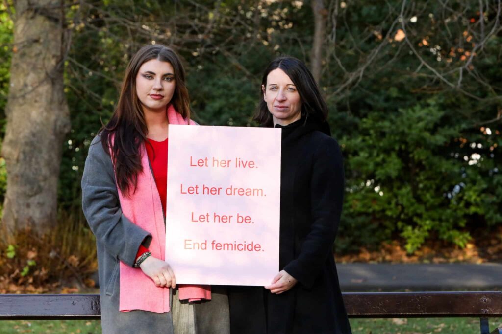 Two women holding a sign reading Let her live. Let her dream. Let her be. End femicide in a park setting.