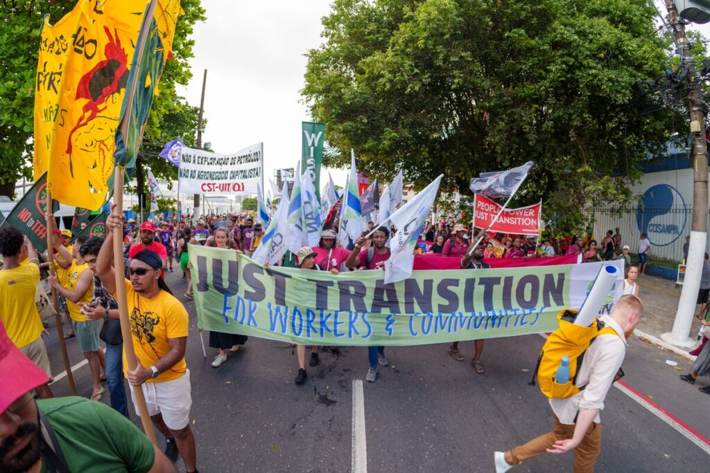 Protest march for climate justice and fair transition for workers and communities, banners and flags displayed.