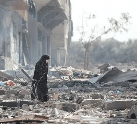 Person in dark clothing walking through rubble of a damaged building, symbolizing destruction and resilience.