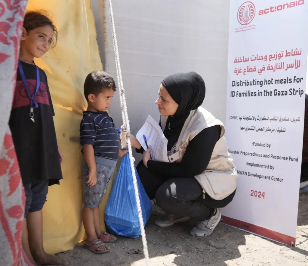 Volunteer distributing meals to children in Gaza, standing beside a sign, during a humanitarian aid effort.