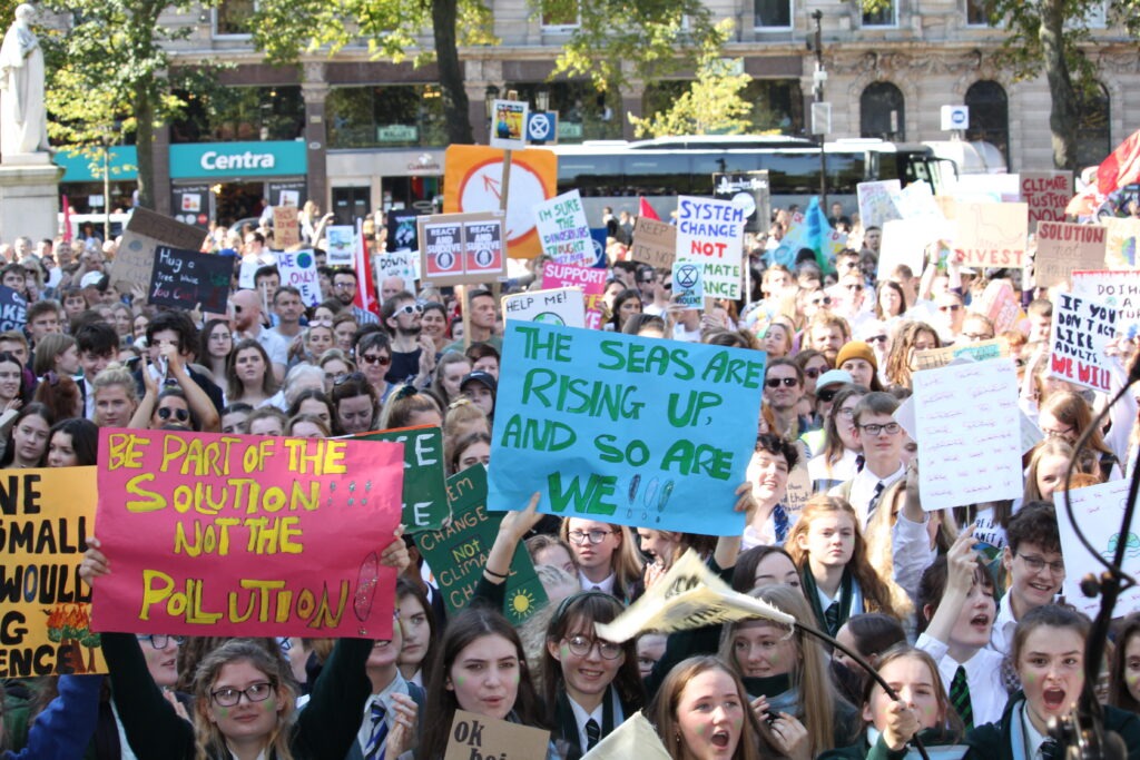 Climate protest with diverse crowd holding signs about environmental action in a city square.