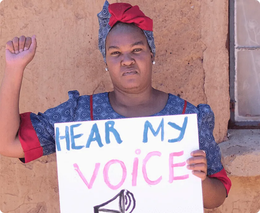 Protester holds Hear My Voice sign, raising fist for empowerment and equality, wearing traditional attire.