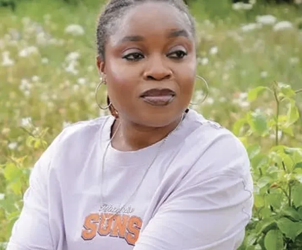 Person in a casual Suns shirt sitting in a lush green field, surrounded by wildflowers, looking contemplative.