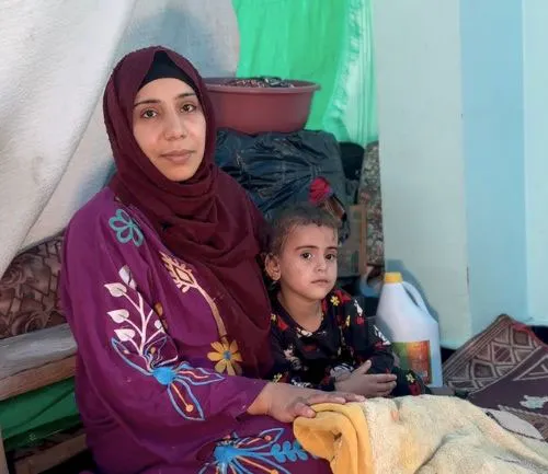 Woman and child sitting in a tent, surrounded by household items, conveying warmth and resilience.