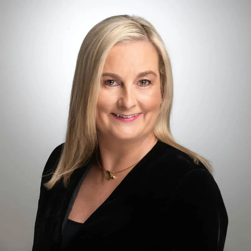 Portrait of a smiling woman with blonde hair in a black top, neutral background.