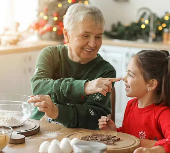 Grandmother and granddaughter baking together in a festive kitchen, smiling and enjoying holiday preparations.