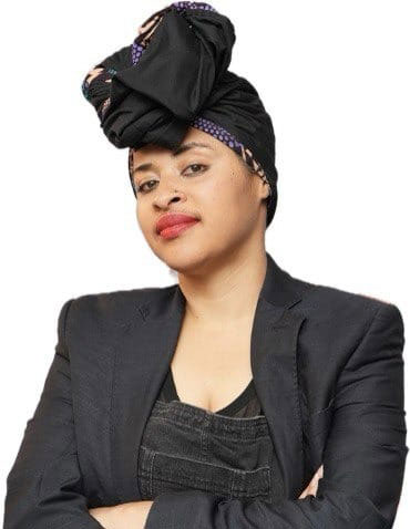 Confident person wearing a headwrap and blazer, looking forward with arms crossed against a white background.
