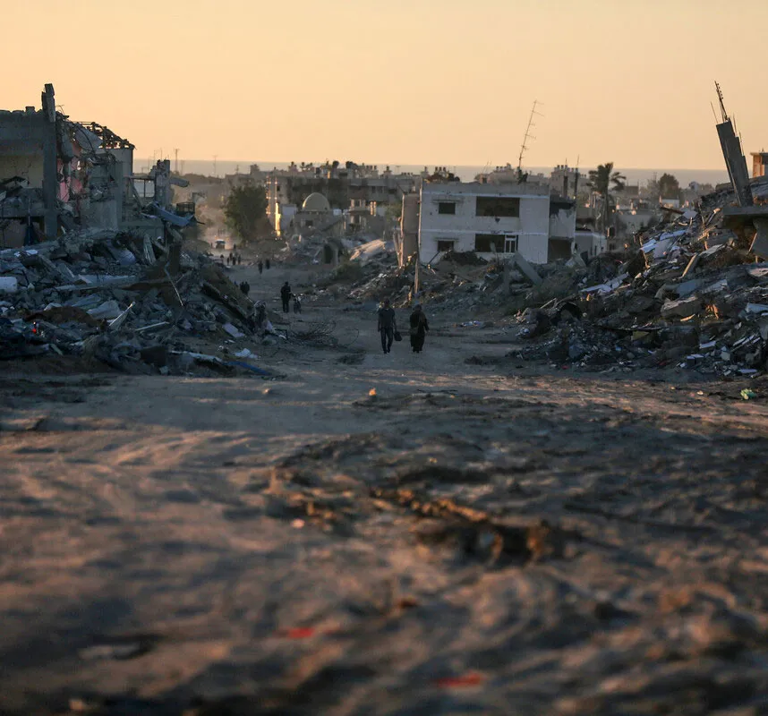 Post-apocalyptic urban landscape at sunset, with people walking amidst rubble and destroyed buildings.