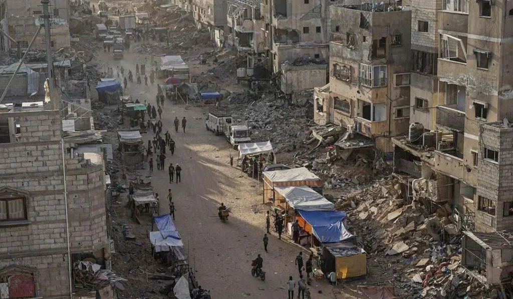 Bustling street amidst war-torn buildings, with makeshift stalls and people navigating debris.