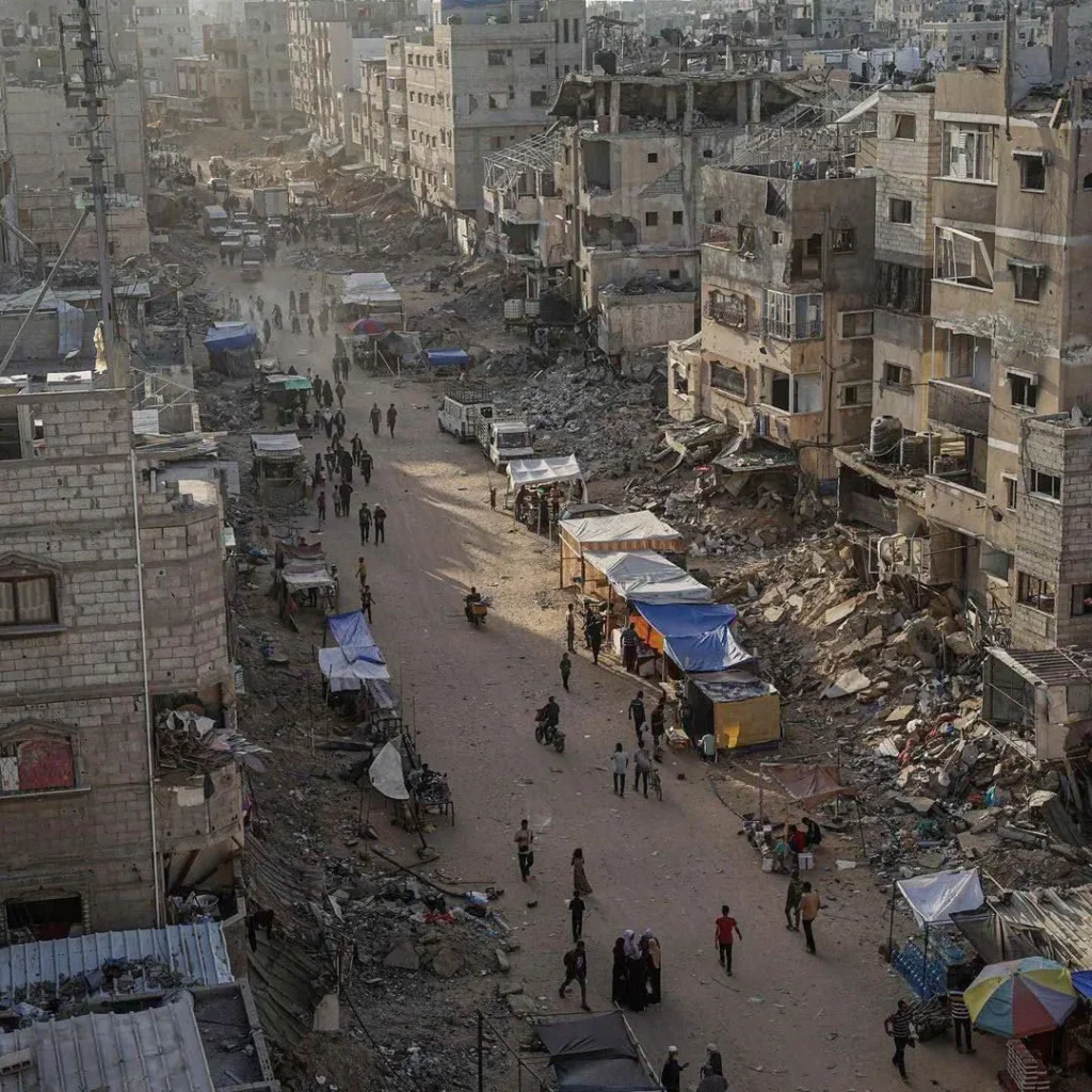 Street amidst rubble and damaged buildings, with people and market stalls, depicting aftermath of devastation.