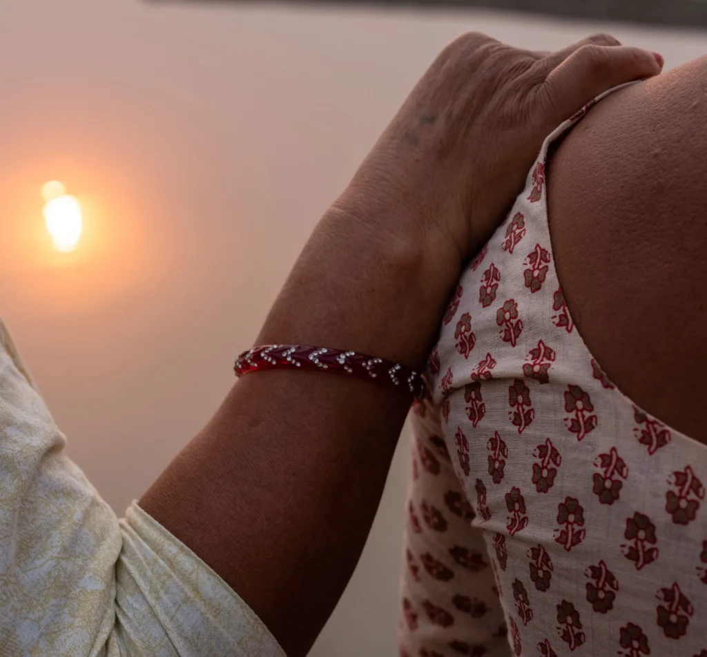 Hand on shoulder at sunset, wearing floral pattern fabric, symbolizing support and companionship in a serene setting.