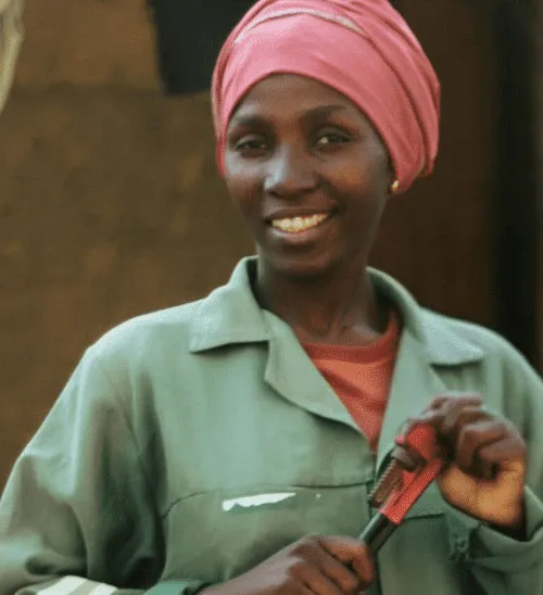 Smiling woman in work attire holding a tool, promoting women in skilled trades.