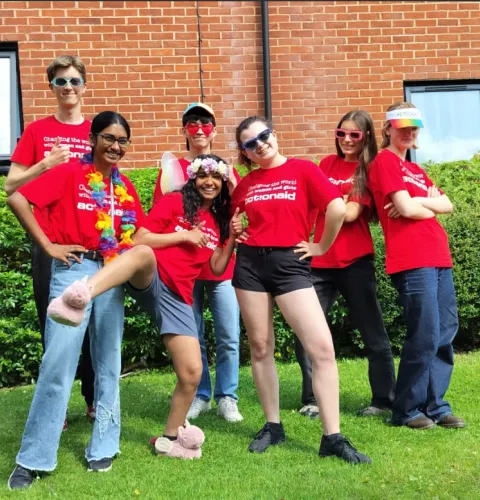 Group of smiling people in red shirts posing outdoors with playful accessories, showing team spirit and diversity.