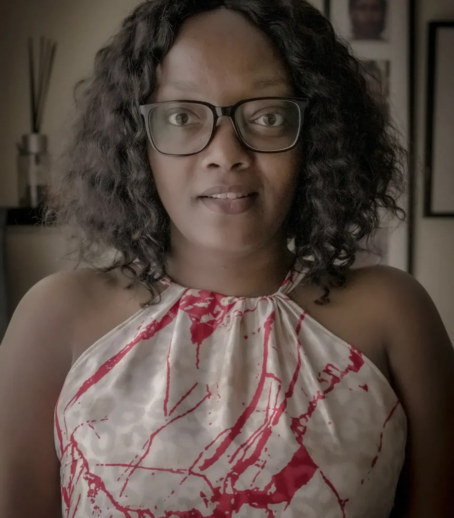 Person wearing glasses and a red-patterned top, posing indoors with a neutral expression.