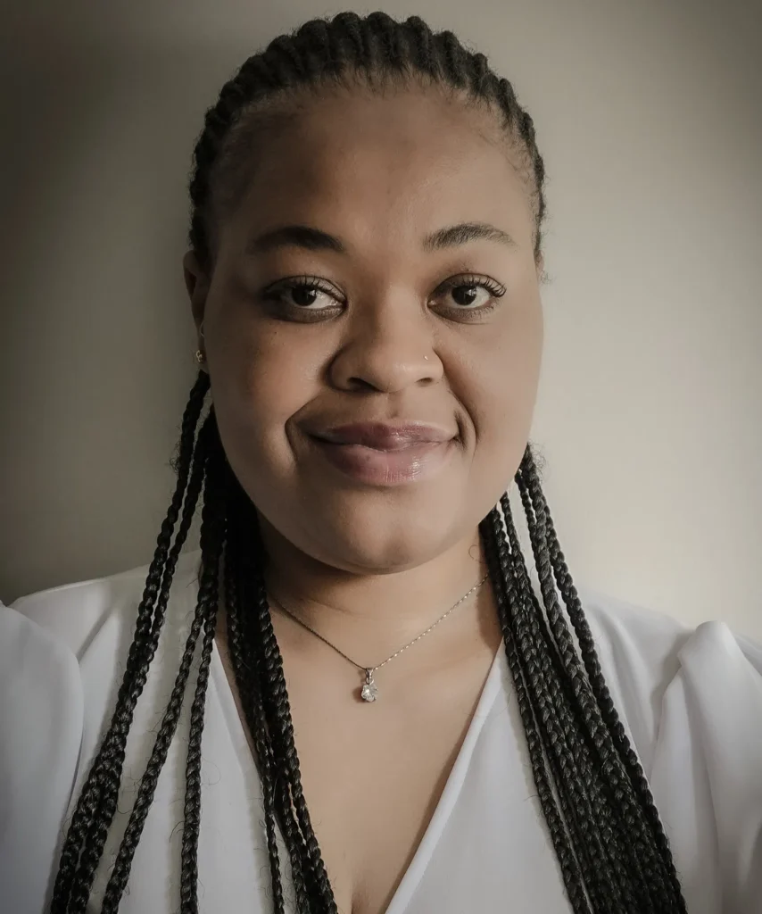 Portrait of a smiling individual with braids and a white blouse, wearing a pendant necklace.