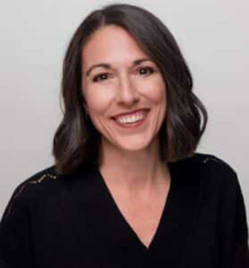 Smiling woman with shoulder-length brown hair in a black top against light background.